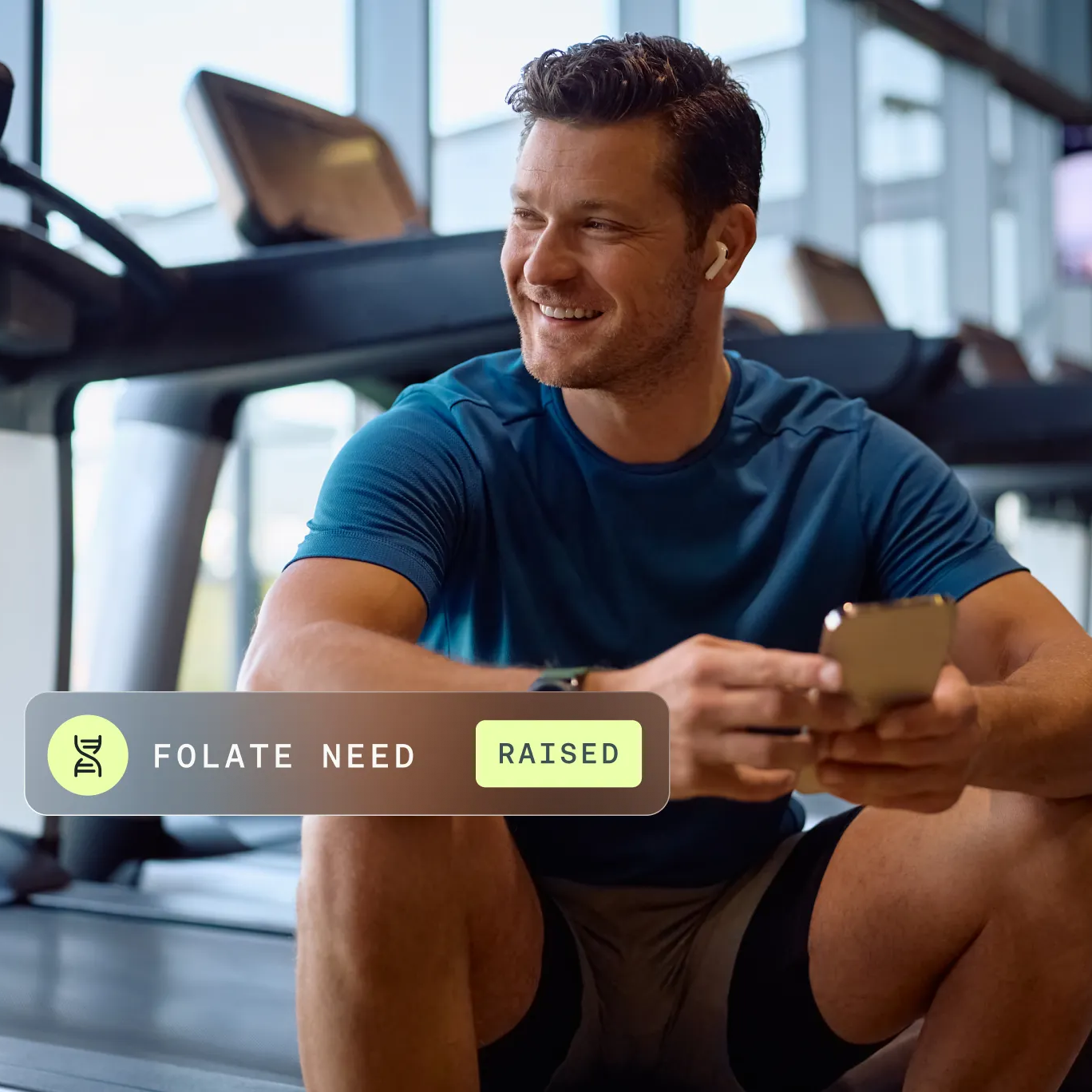 Man sitting on a gym bench using a smartphone with a fitness app notification about folate need.